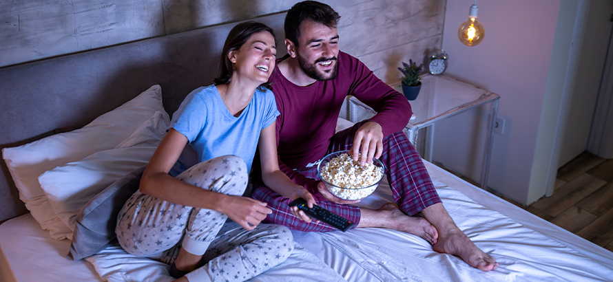 Mann und Frau lachen beim gemeinsamen Filmabend im Bett