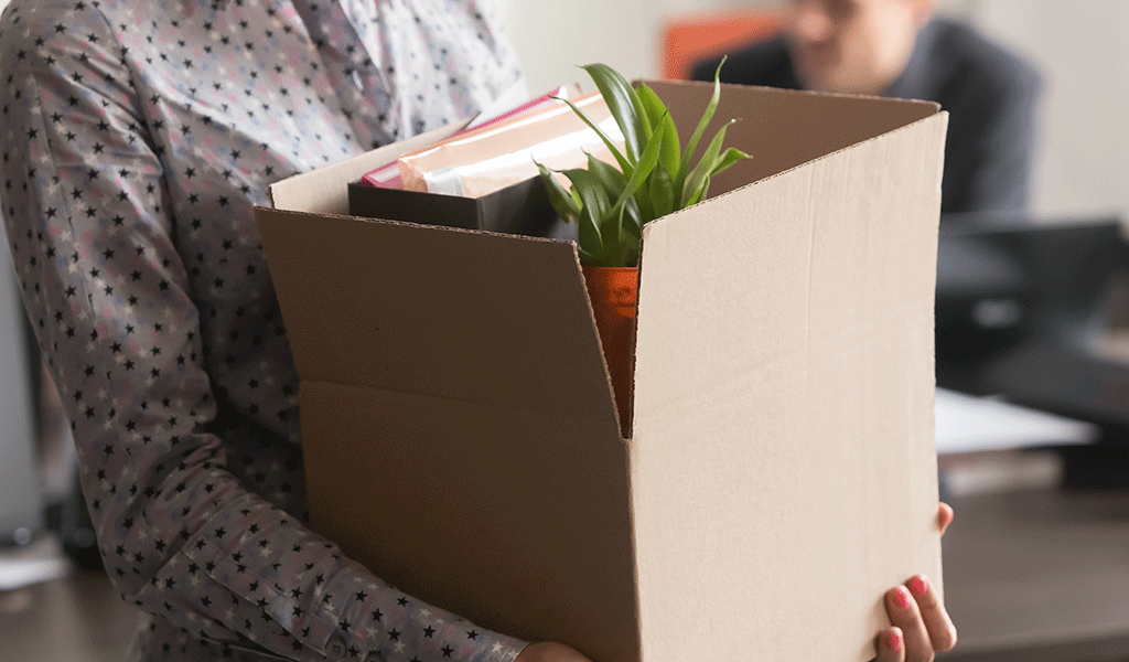 Frau verlässt Büro mit Karton, nachdem sie gegangen worden ist