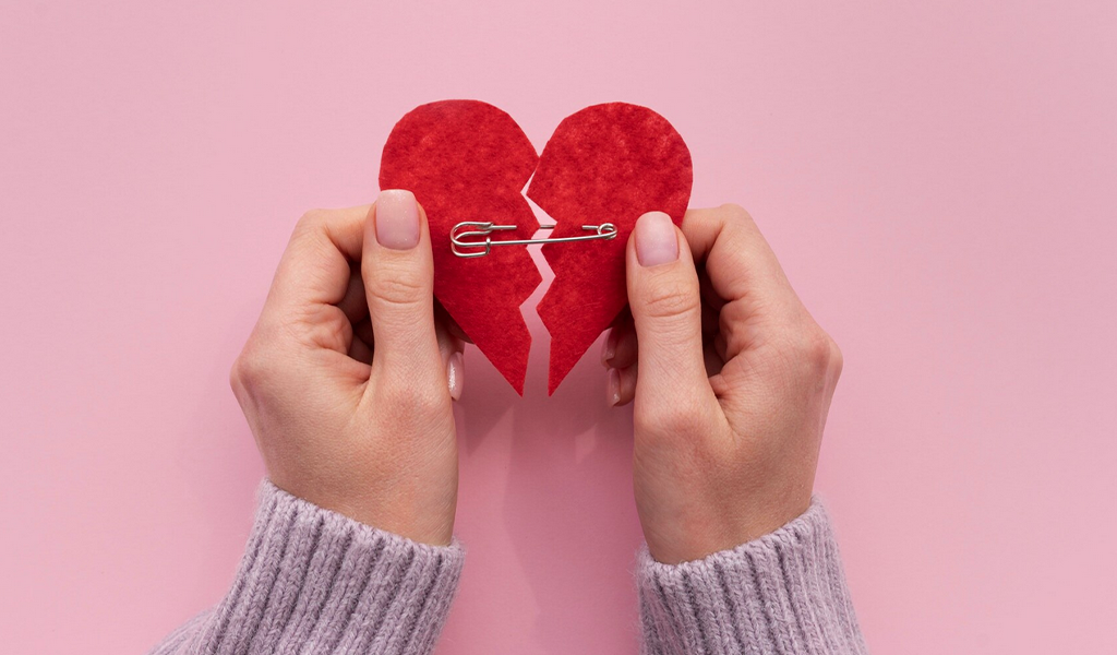 Frau hält gebrochenes Herz mit beiden Händen zusammen
