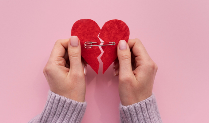 Frau hält gebrochenes Herz mit beiden Händen zusammen