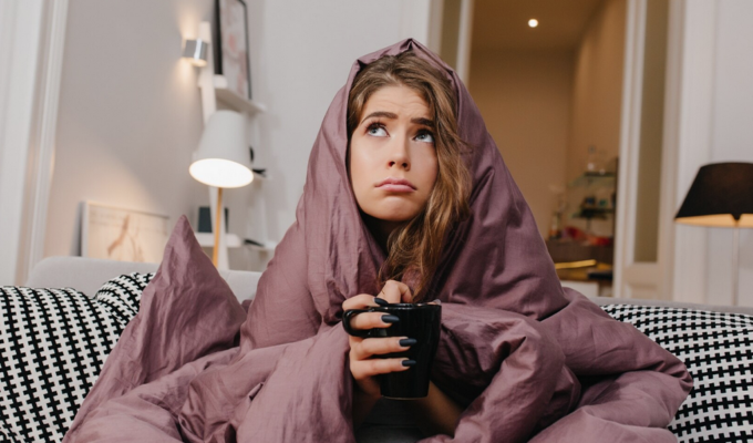 Frau kuschelt sich in Decke ein mit Teetasse